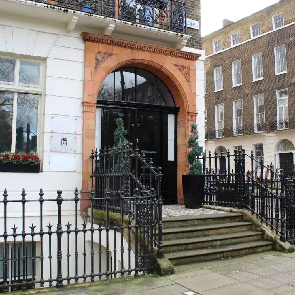 The entrance to the building: a black front door under a red-brick arch, with railings and steps up from a Georgian street