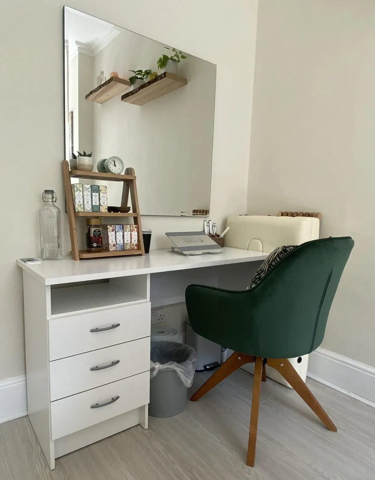 A white desk with a green chair and a mirror in the corner of the room
